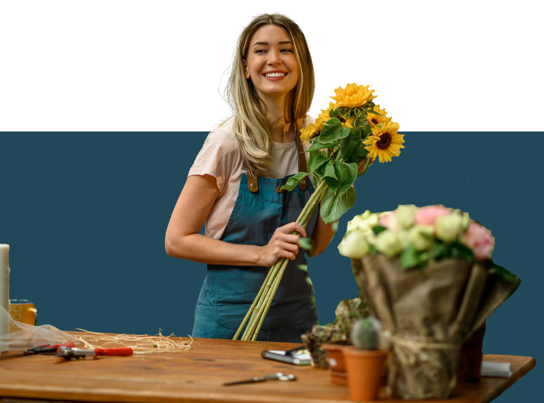 A woman is standing at a table holding a bouquet of flowers.