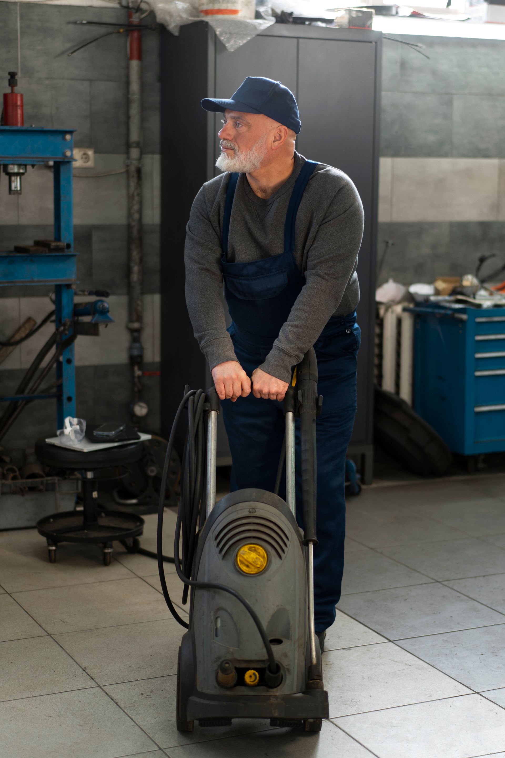 An older man is standing next to a high pressure washer in a garage.