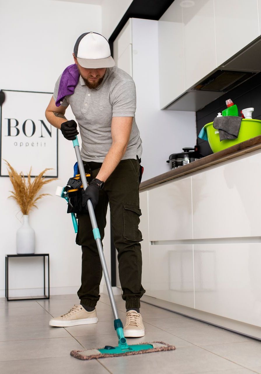 A man is cleaning the floor of a kitchen with a mop.
