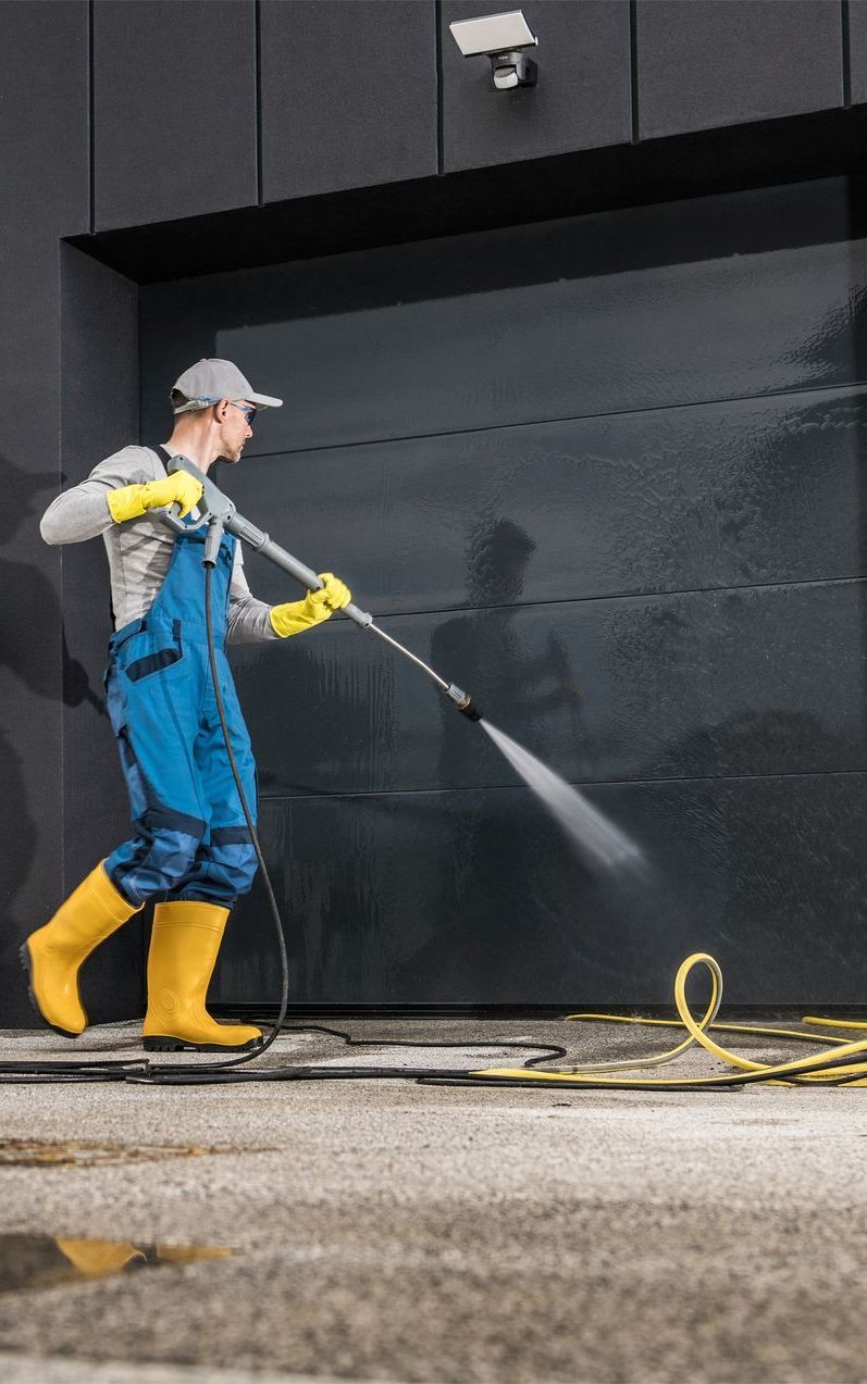 A man is cleaning a garage door with a high pressure washer.