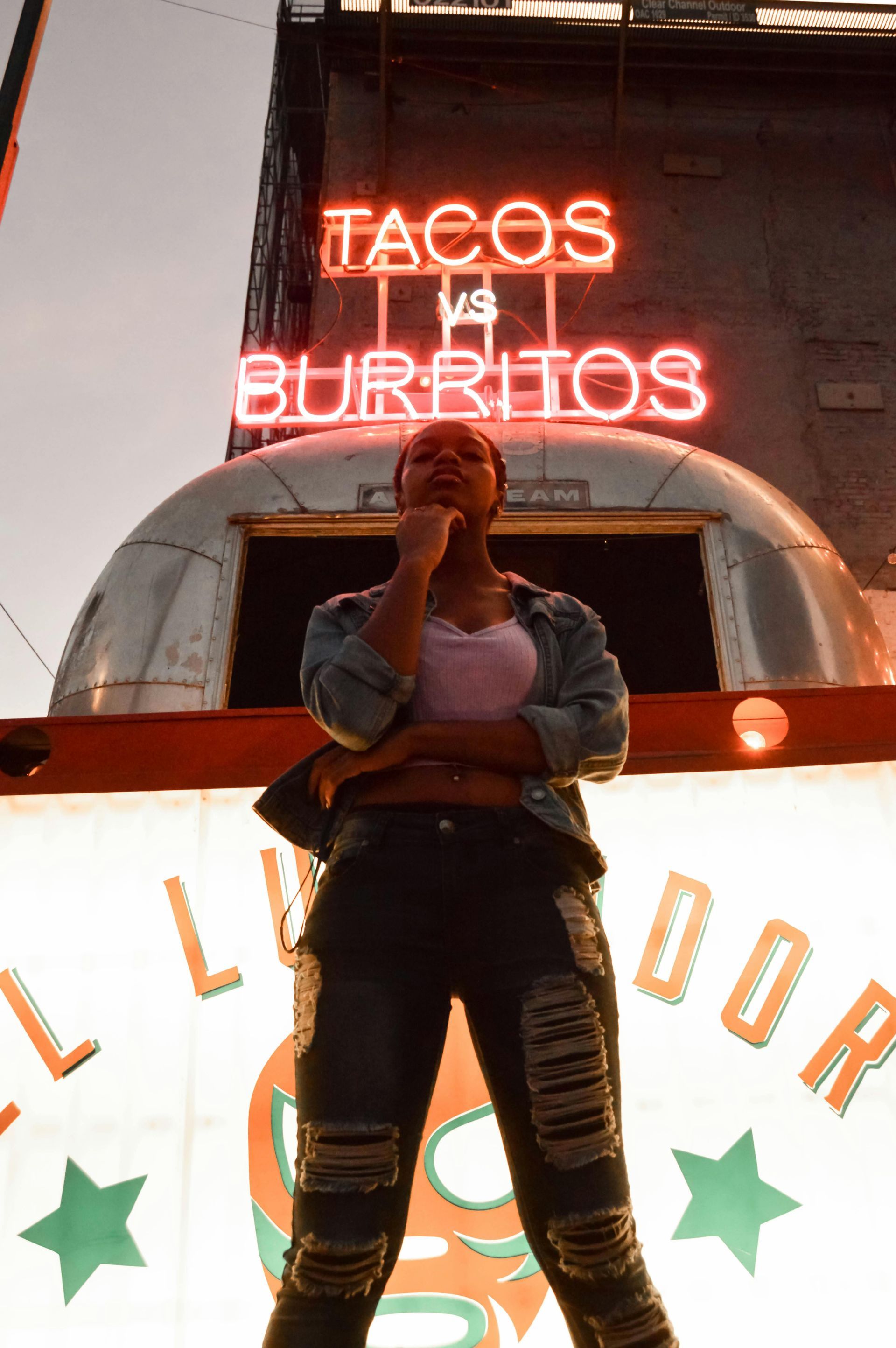 A woman is standing in front of a tacos and burritos sign.
