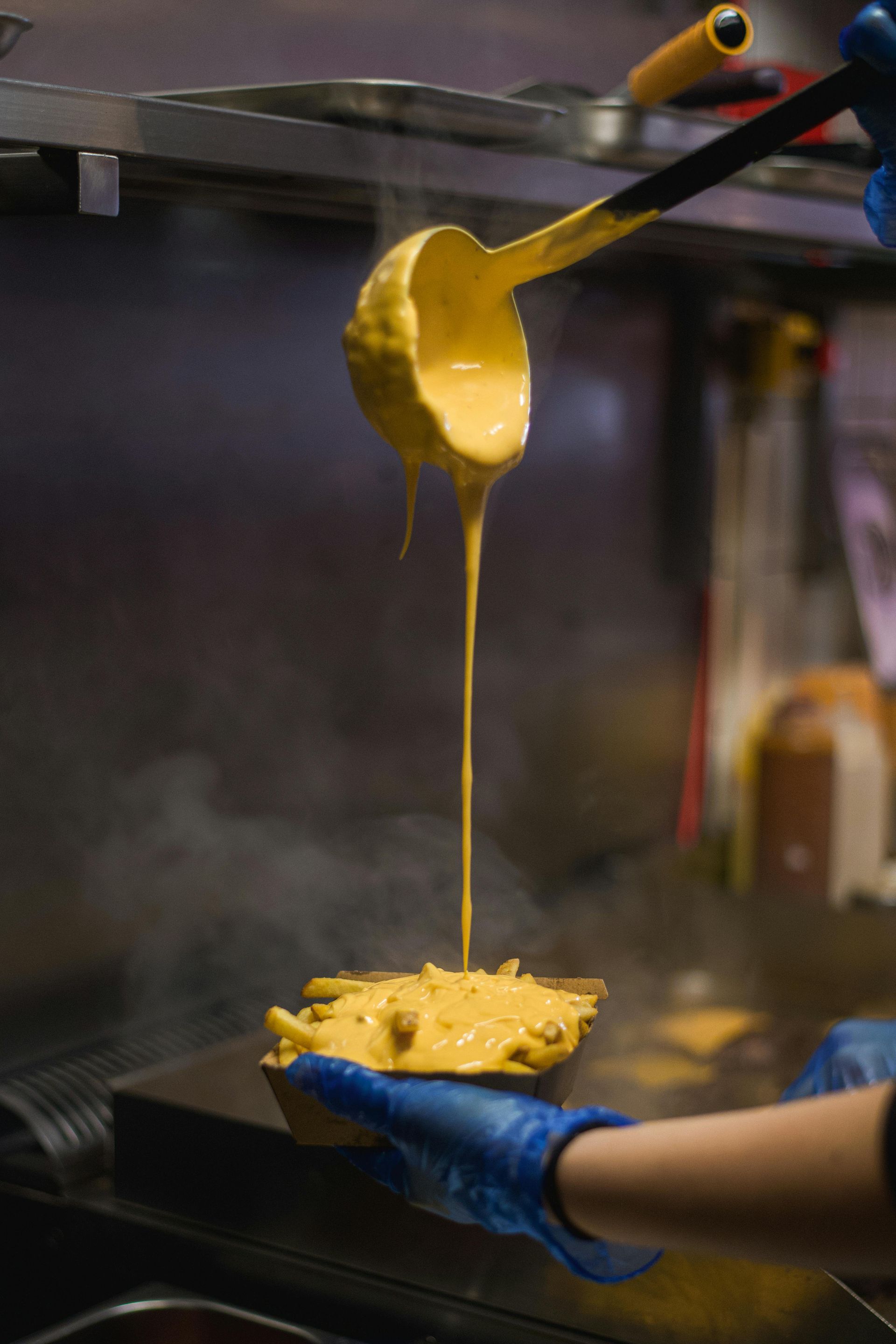 A person is pouring cheese into a bowl of french fries.