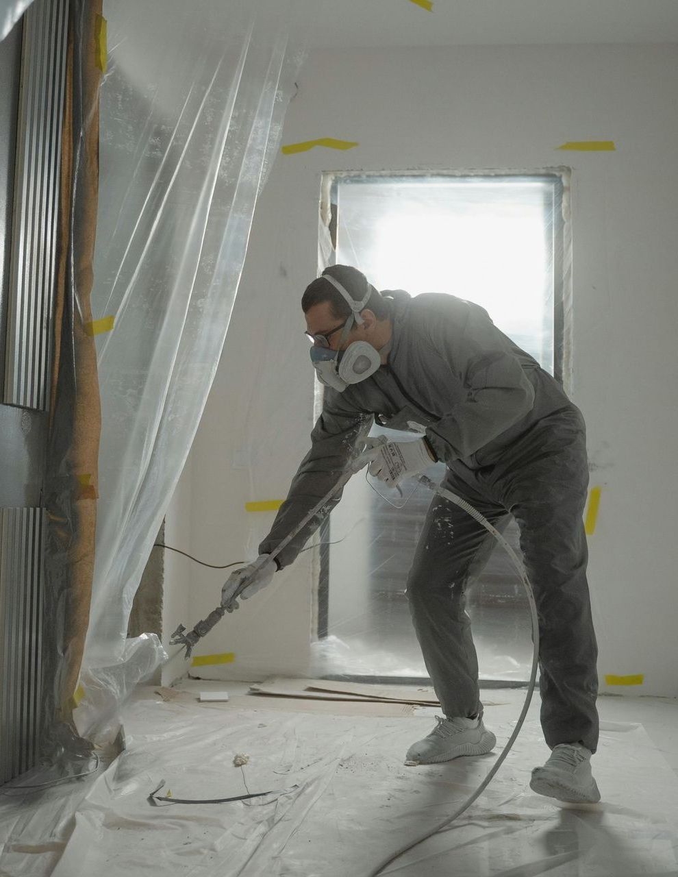 A man wearing a mask is spray painting a wall in a room.