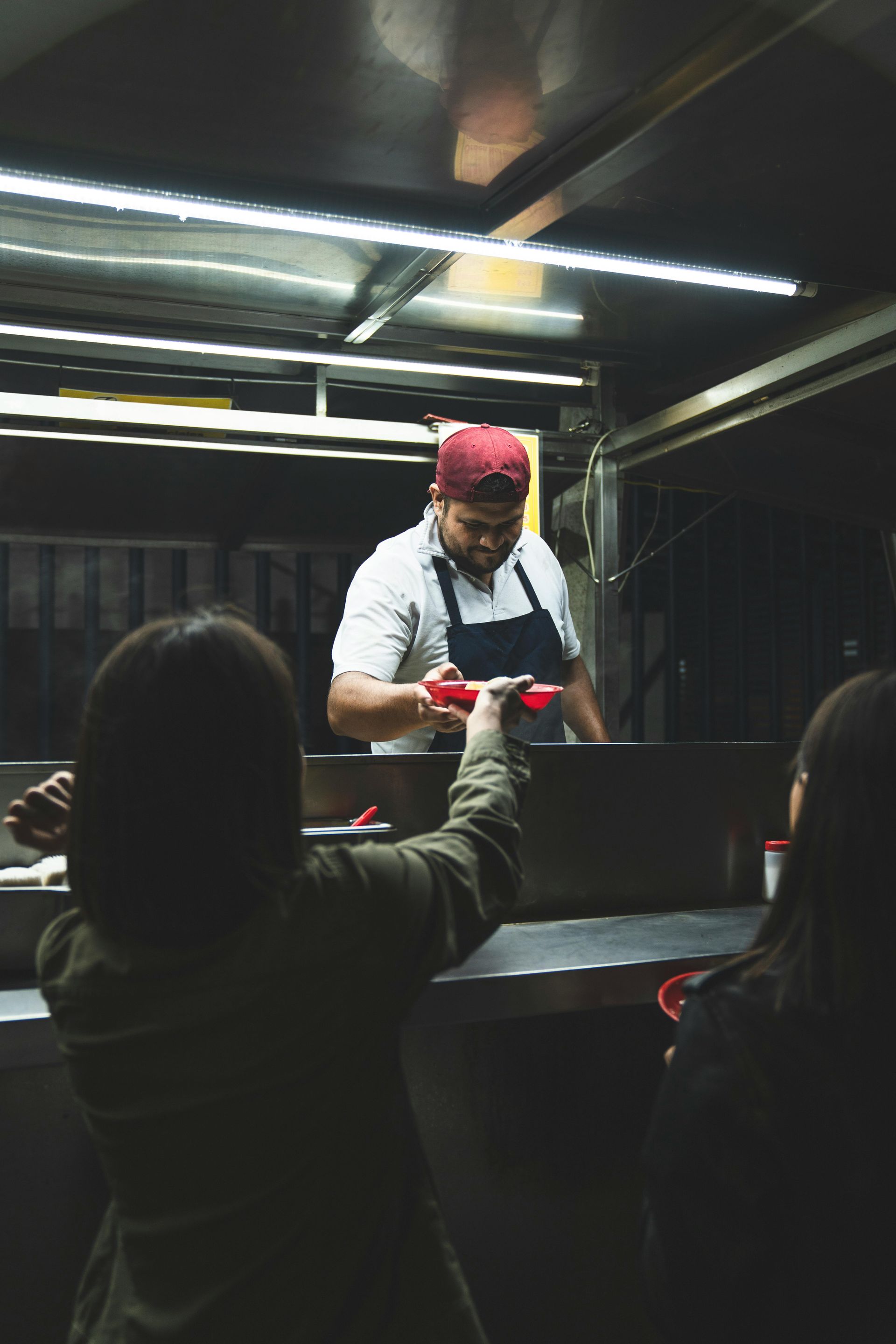 A man is cooking food in a food truck while a woman looks on.