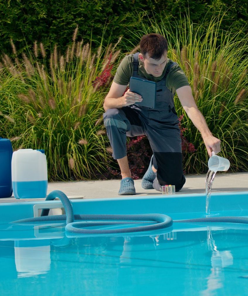 A man is pouring water into a swimming pool while using a tablet.