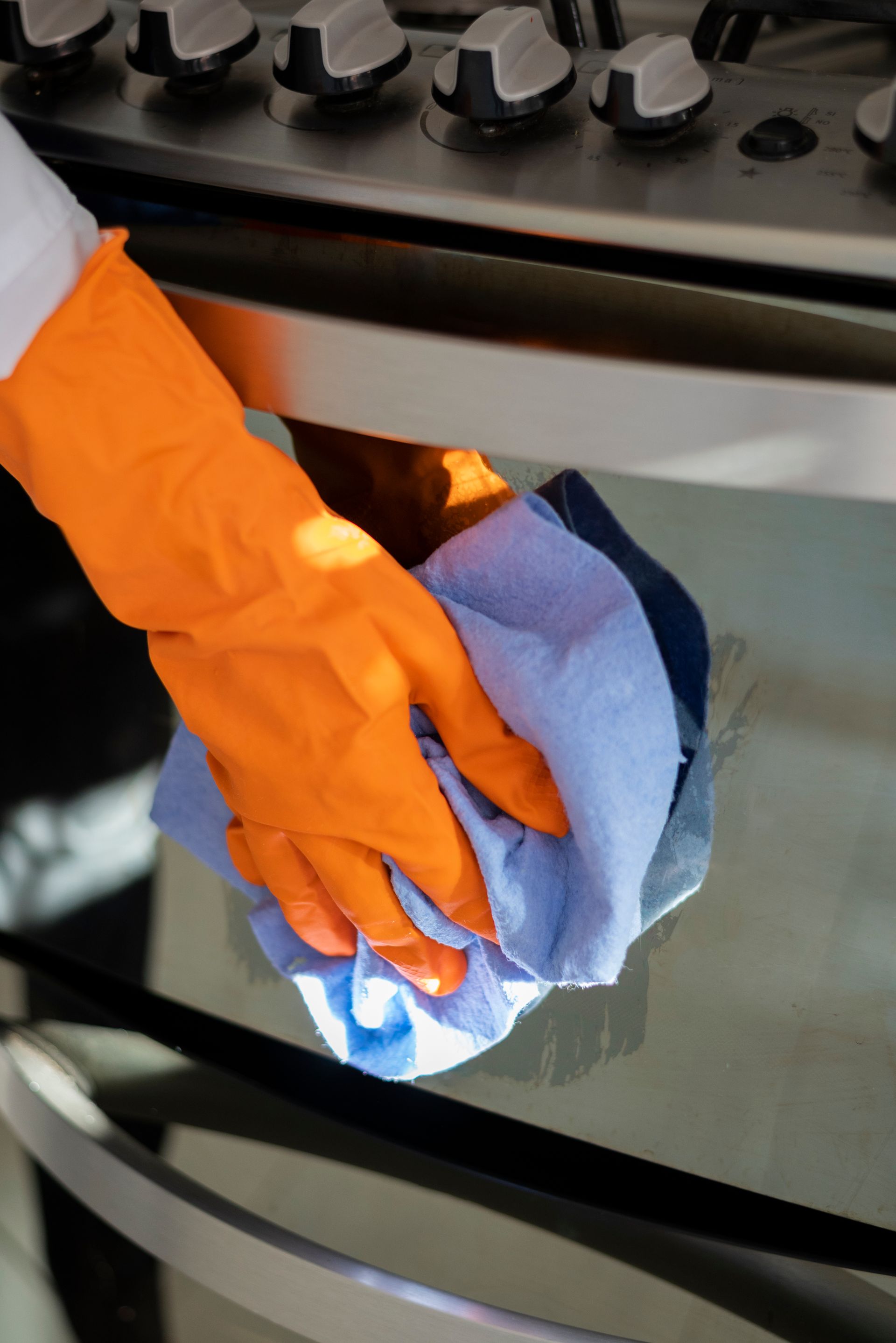 A person wearing orange gloves is cleaning an oven with a cloth