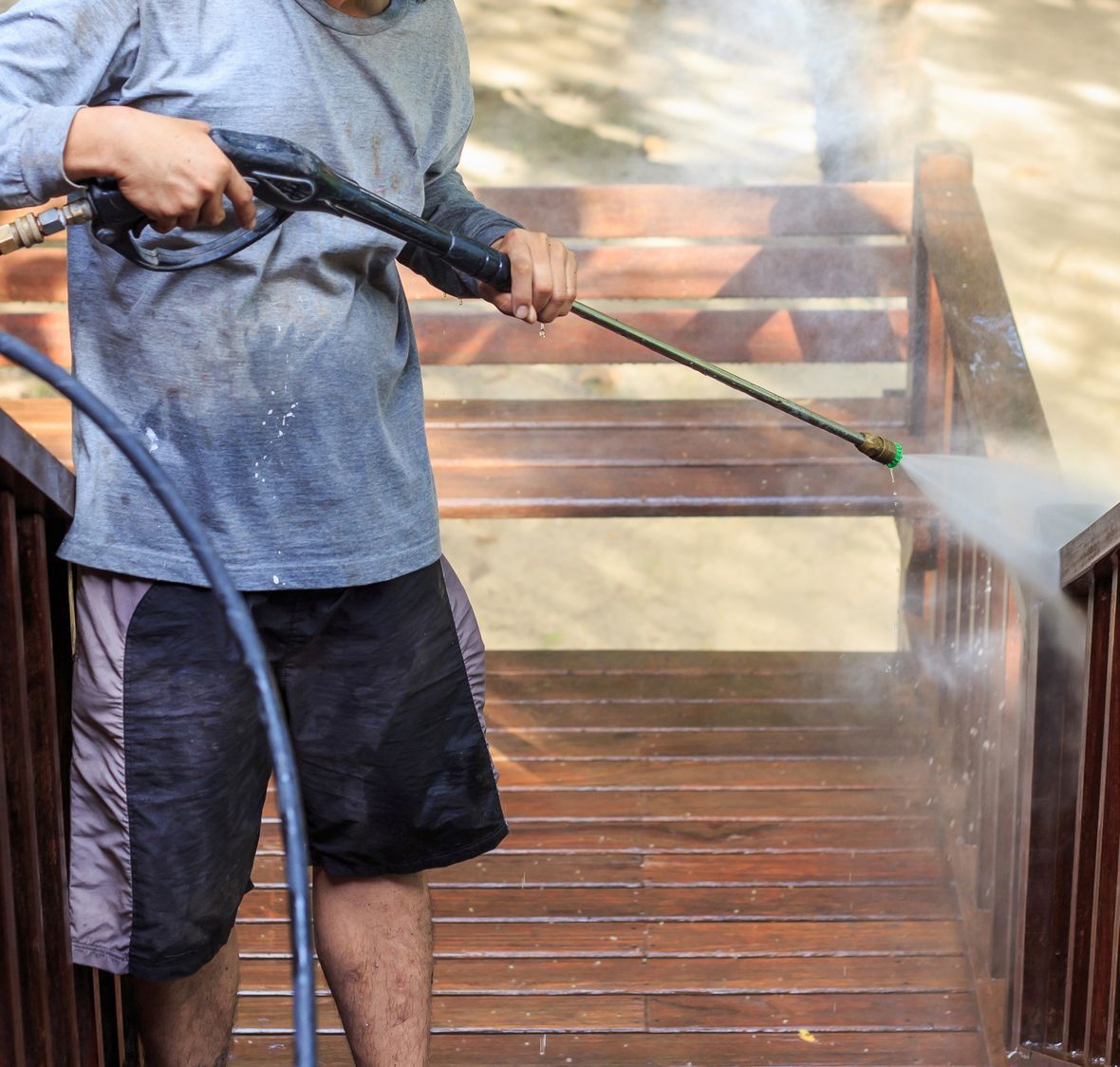 A man is using a high pressure washer to clean a wooden deck