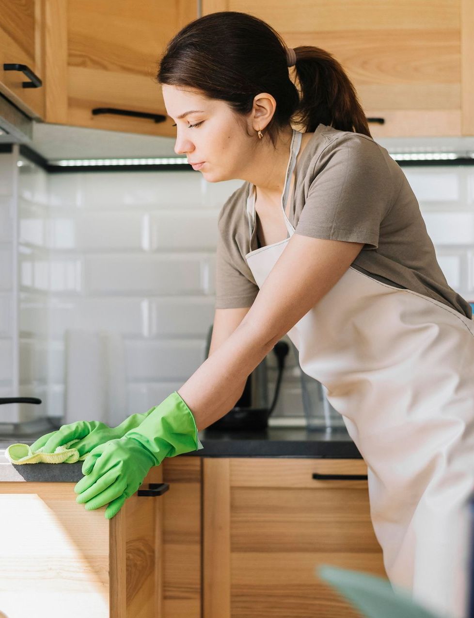A woman wearing green gloves is cleaning a kitchen counter.