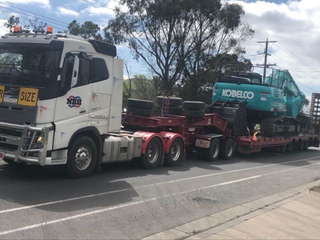 A large truck is carrying a kobelco excavator on a trailer.