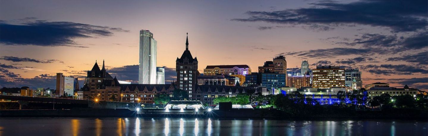 City skyline at dusk with illuminated buildings and reflections on calm water
