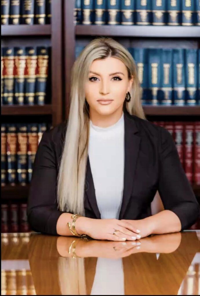 Professional woman seated at a desk in front of law books, facing the camera
