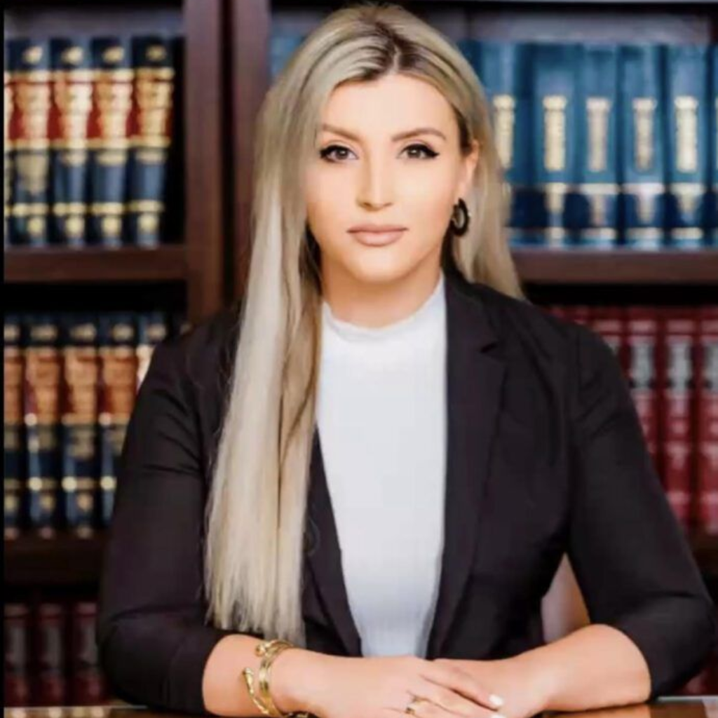 Portrait of a blonde professional in a black blazer seated before law books in a library setting