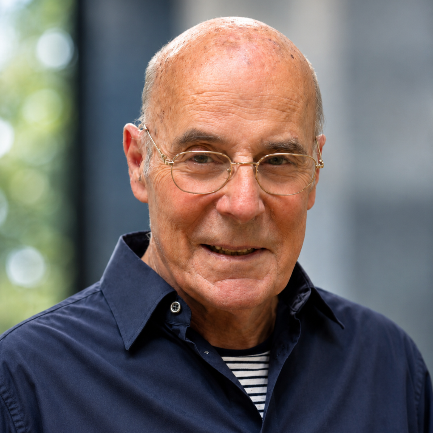 Portrait of a bald man with glasses in a navy shirt, smiling outdoors.