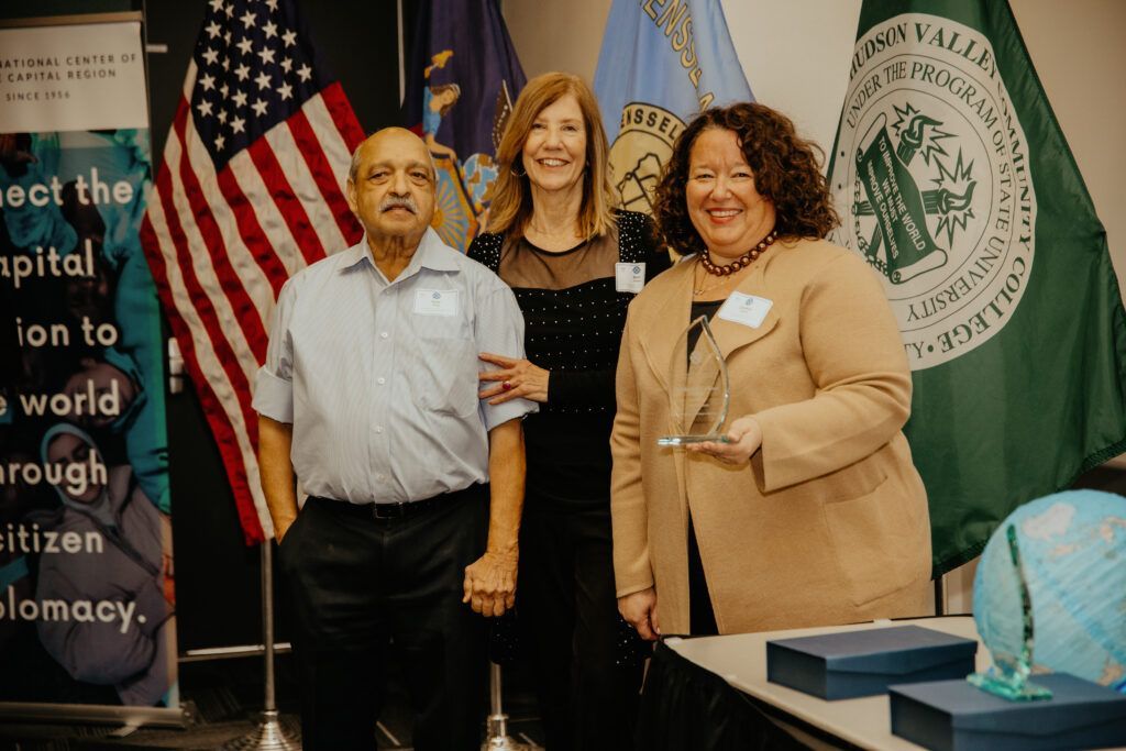 Three people posing at a table with flags and a globe in the background.