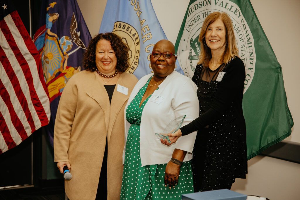 Three people smiling in front of flags at a formal event