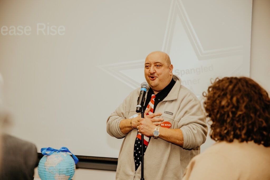Presenter speaking at a microphone in a conference room with an audience seated nearby