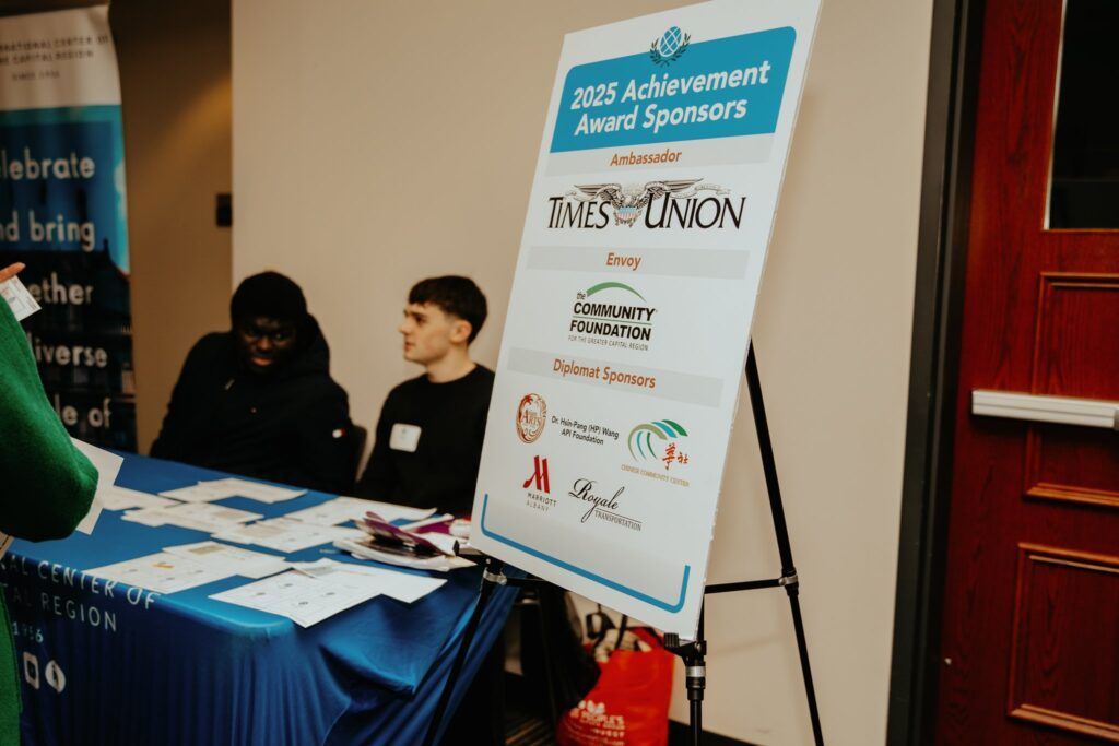 Two people at a blue-draped registration table beside an event signboard at an indoor venue