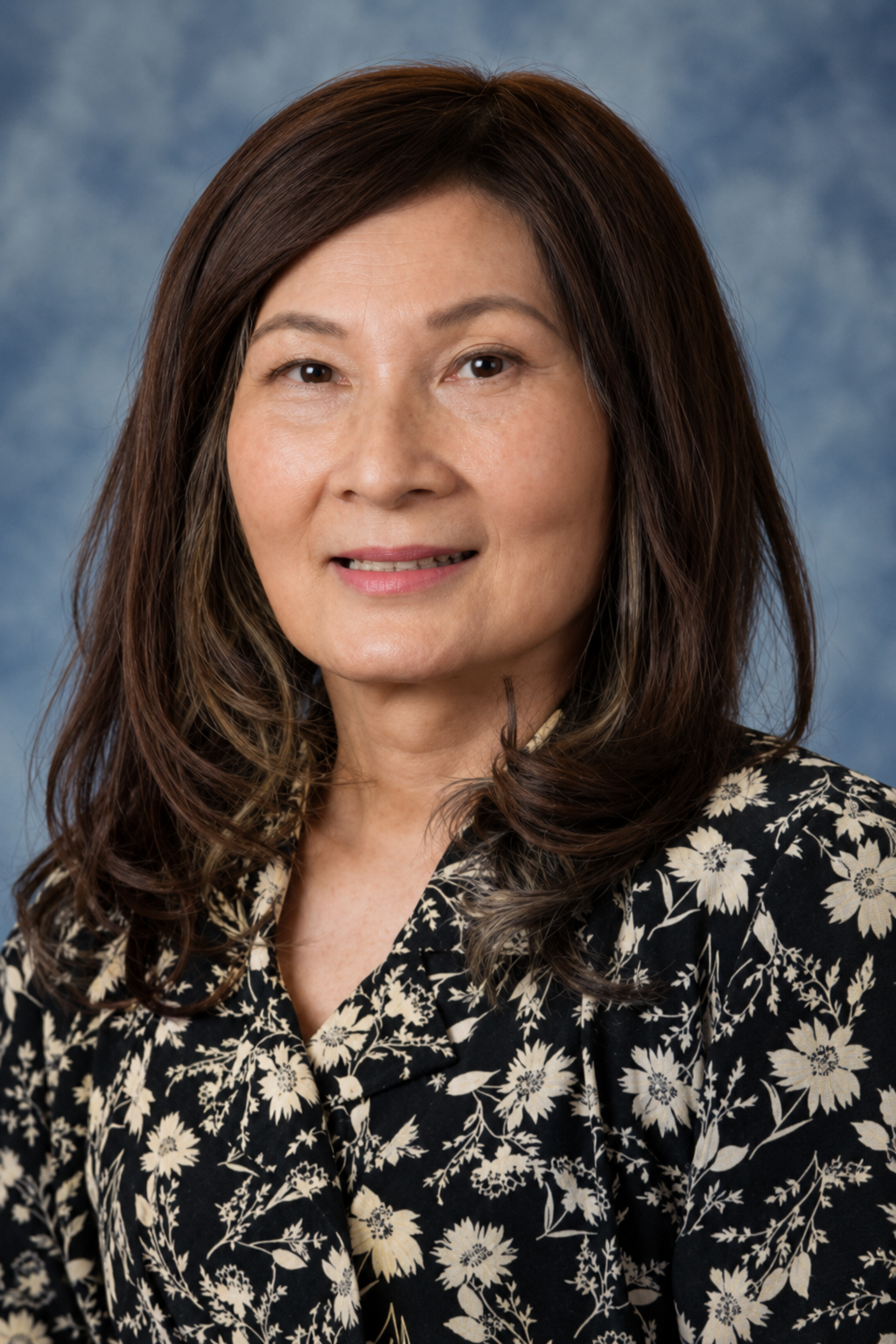 Portrait of a smiling woman with shoulder-length dark hair in a black floral blouse against a blue backdrop