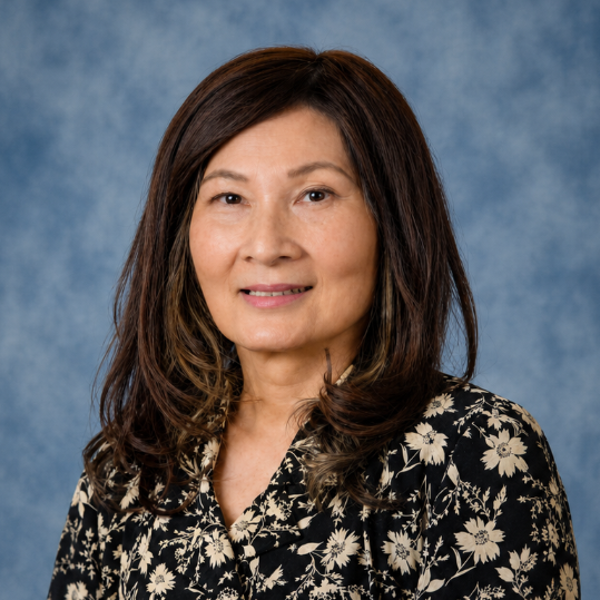 Portrait of a woman smiling in a black floral blouse against a blue studio backdrop
