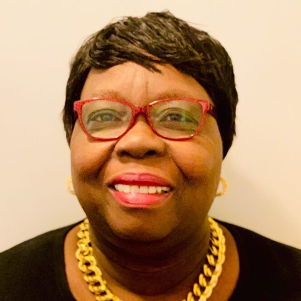 Smiling person wearing red glasses, black top, and gold chain against a light background