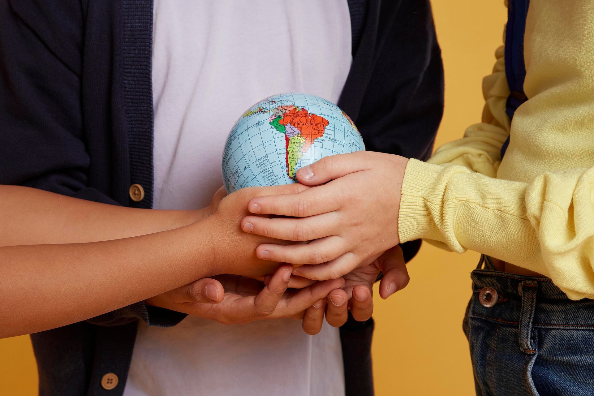 Hands of several people holding a small globe against a yellow background.