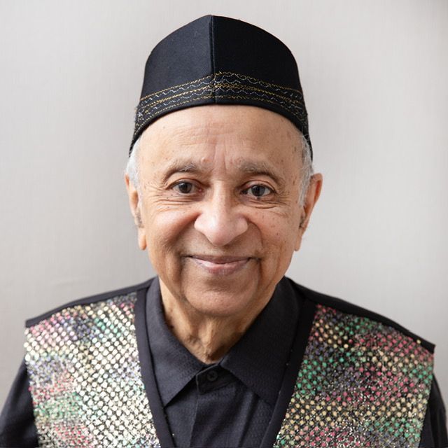Smiling person wearing a black cap and a patterned vest against a light background