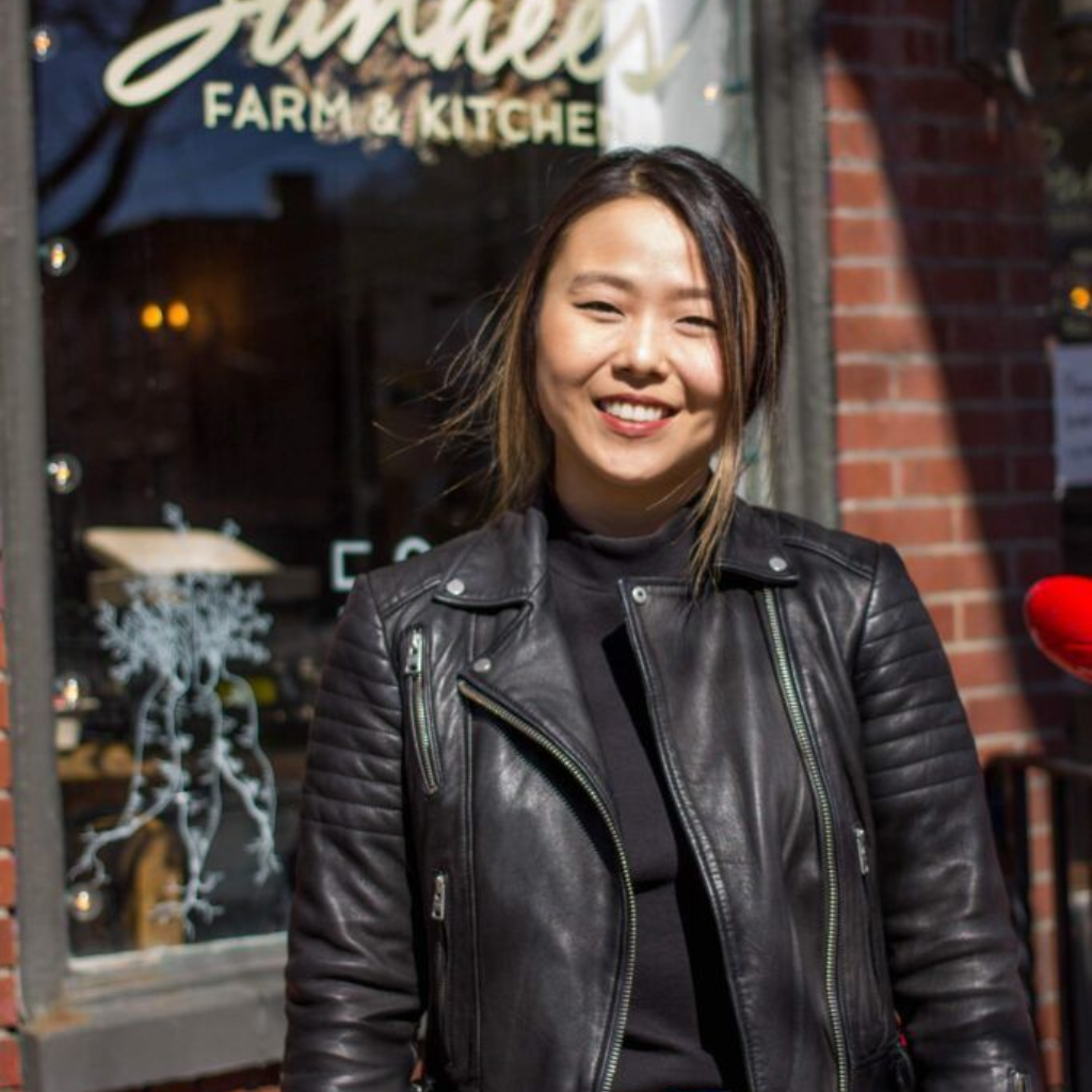 Smiling person in a black leather jacket standing outside a farm-to-kitchen cafe