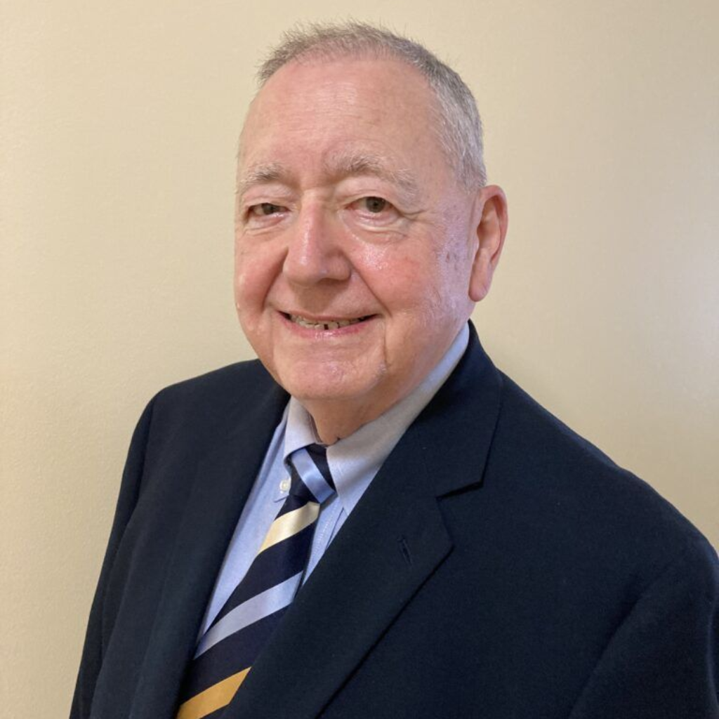Portrait of a smiling man in a dark suit and striped tie against a beige wall