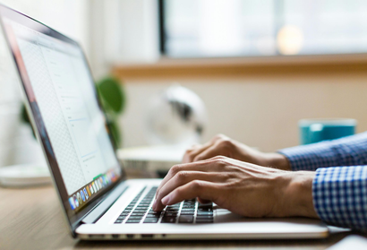 Hands typing on a laptop at a bright desk near a window