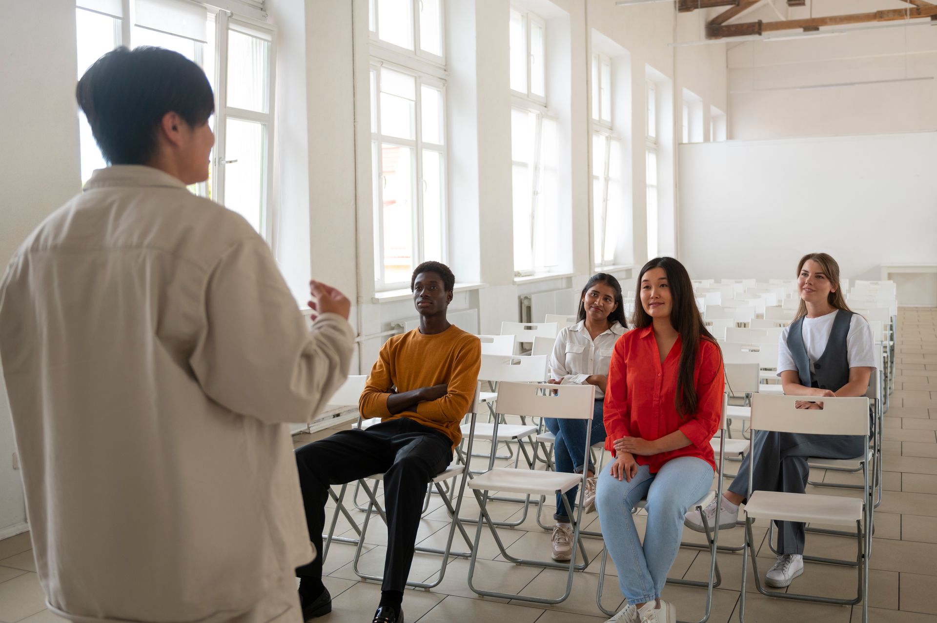 Presenter speaking to a small seated audience in a bright classroom or workshop space