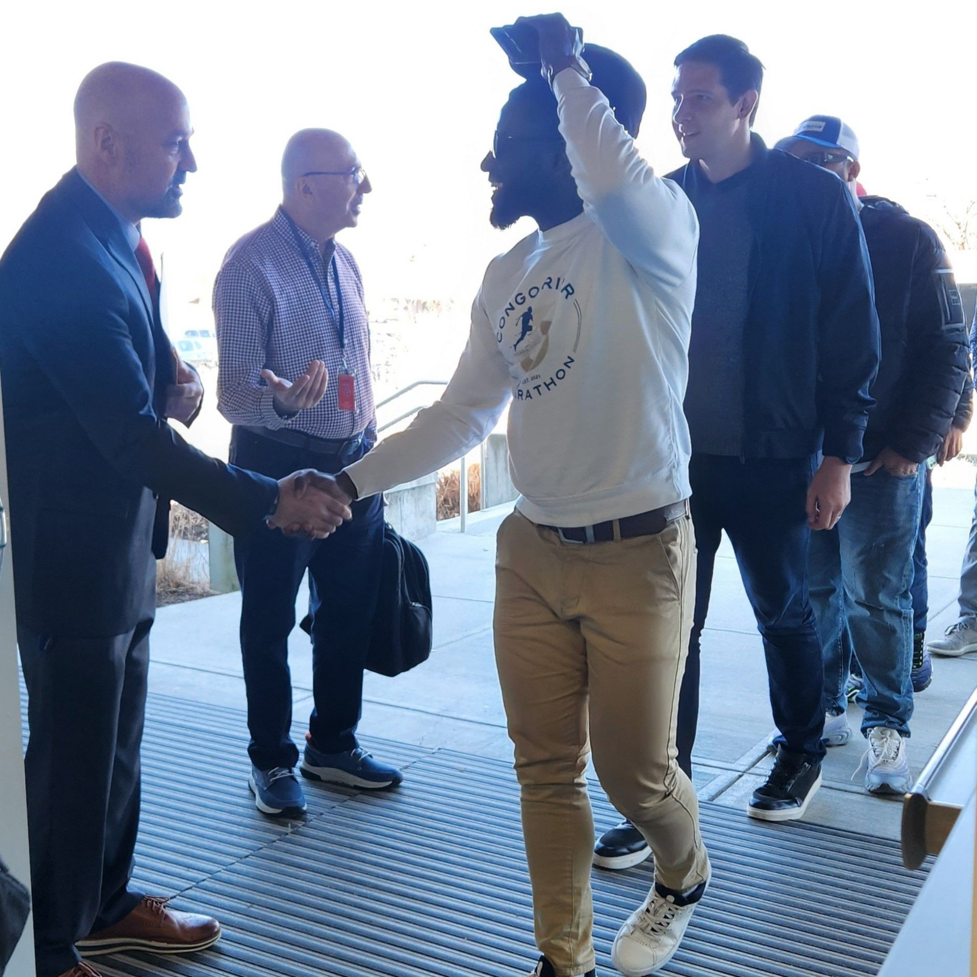 People shaking hands at a doorway as one person carries a bag and raises a jacket overhead