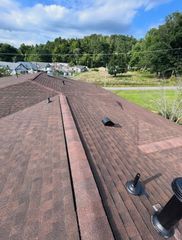 Rooftop with brown shingles, vents, and a view of trees and houses in the distance