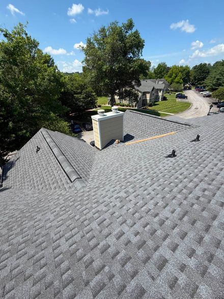 Roof with gray shingles and a small vent, overlooking trees and houses under a blue sky