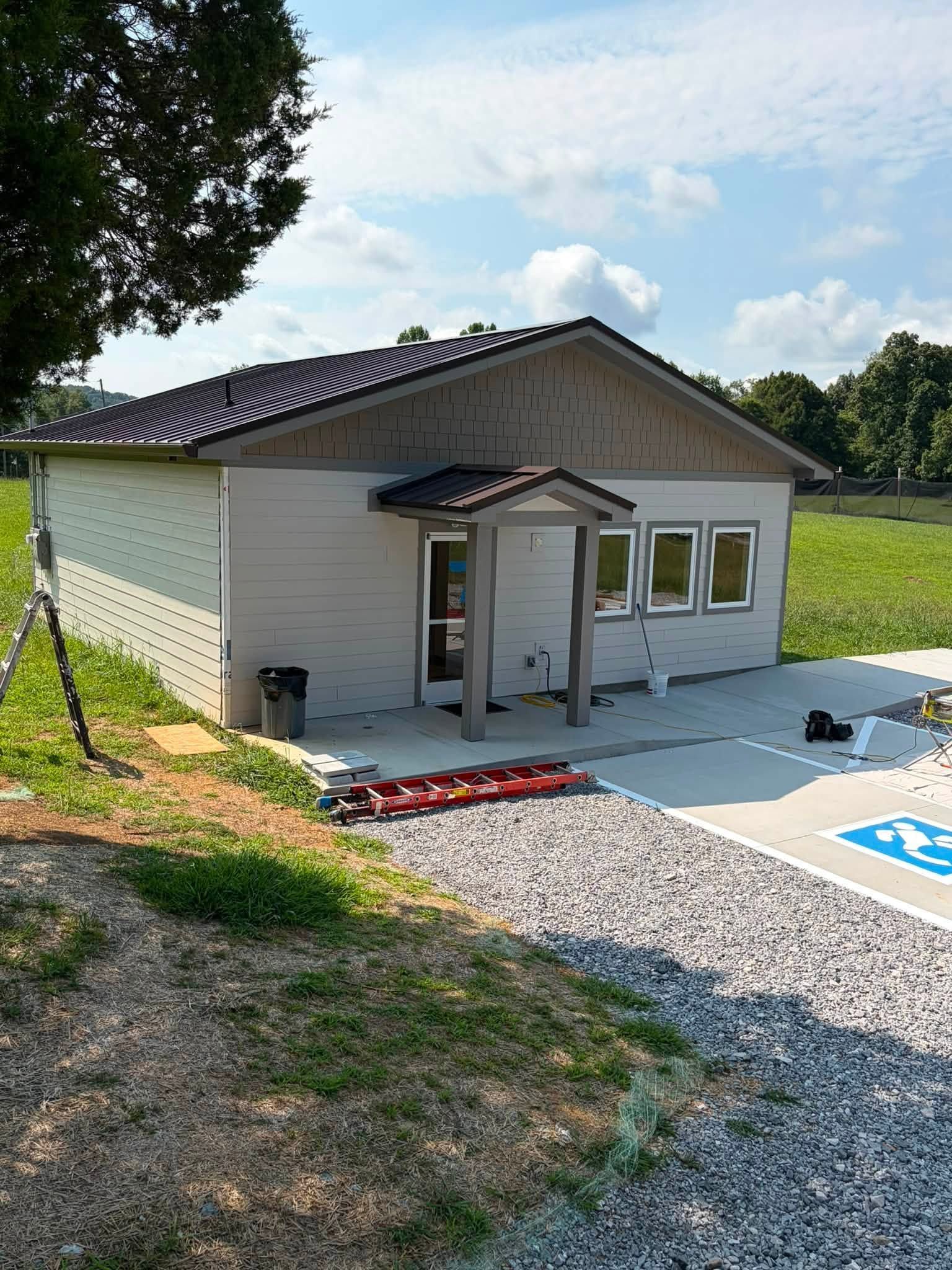 Small white building with a covered entrance beside gravel parking and a handicap space under a blue sky