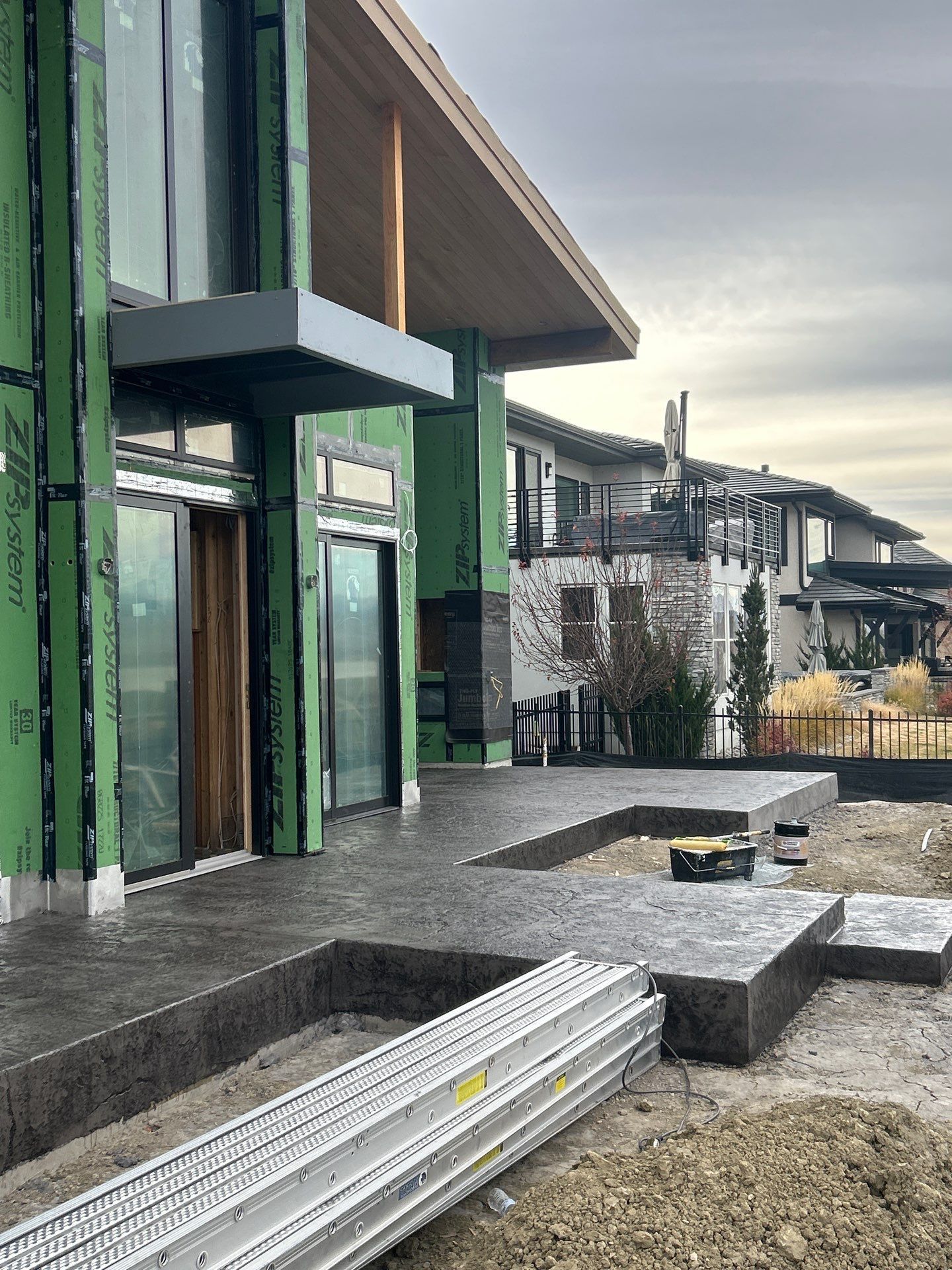Exterior of a modern house under construction; green sheathing, concrete patio, and a cloudy sky.