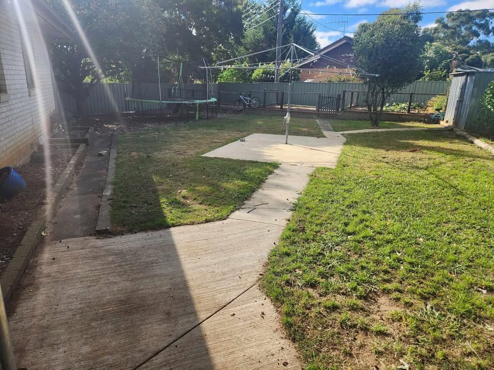 Before A Brick Wall Is Surrounded By Tall Grass And A Fence — Canberra Home and Garden Maintenance in Tuggeranong ACT