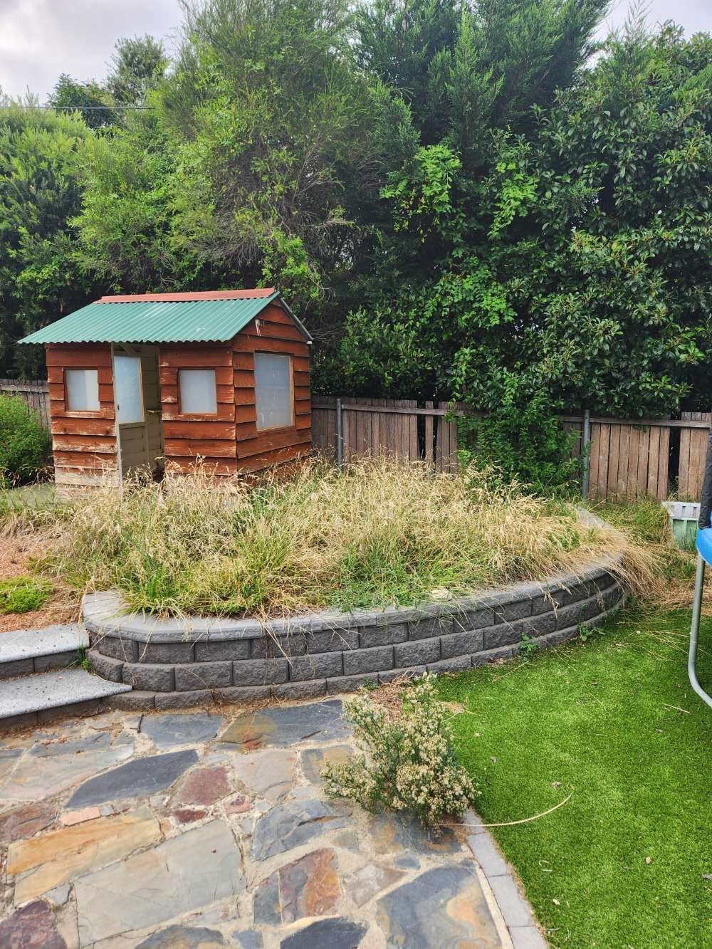Before A small wooden house with a green roof is sitting on top of a grassy hill in a backyard — Canberra Home and Garden Maintenance in Tuggeranong ACT
