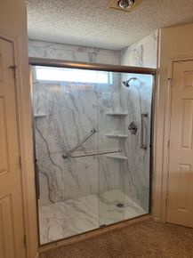 A bathroom with a walk in shower with marble walls and a sliding glass door.