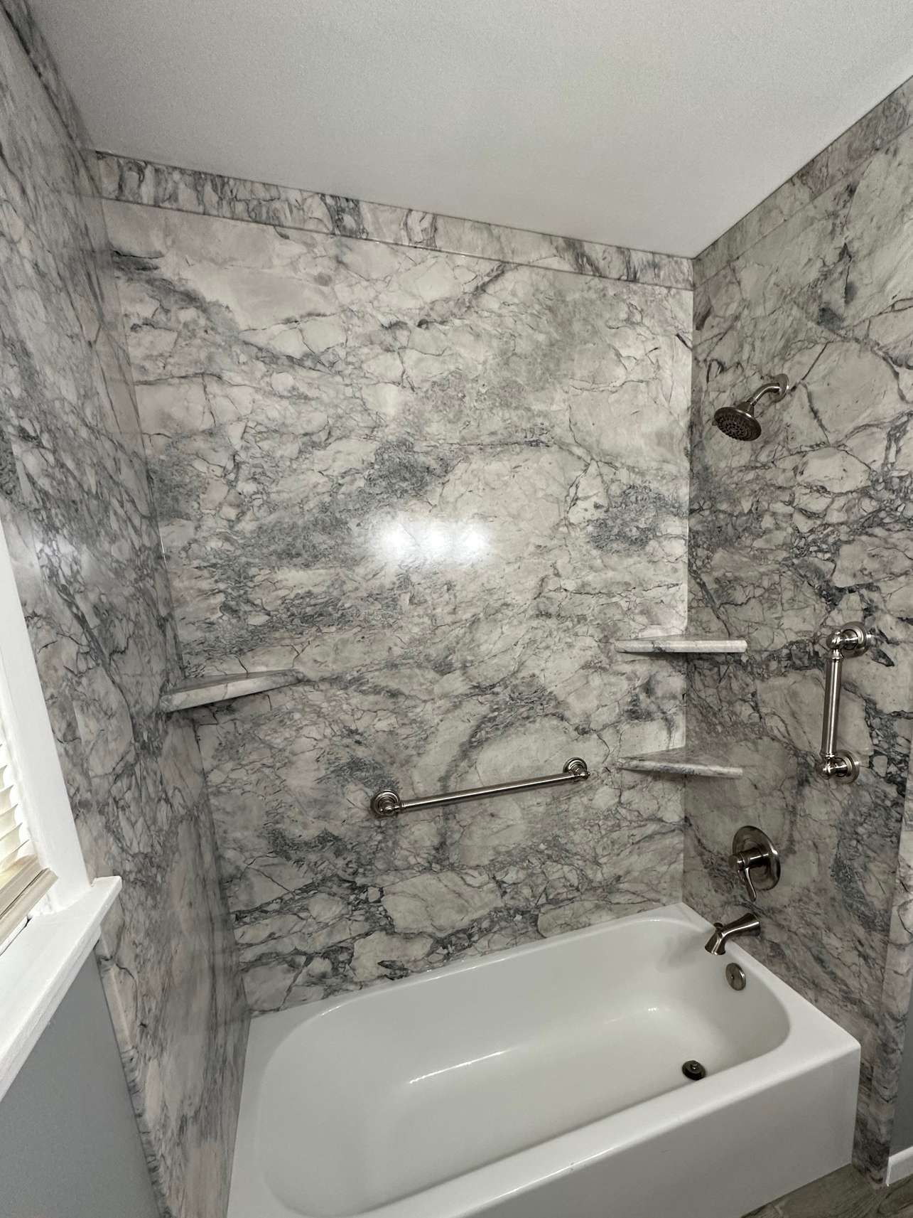 There is a bathtub in the bathroom with marble walls.