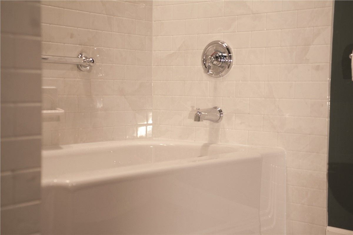 There is a bathtub in the bathroom with white tiles.