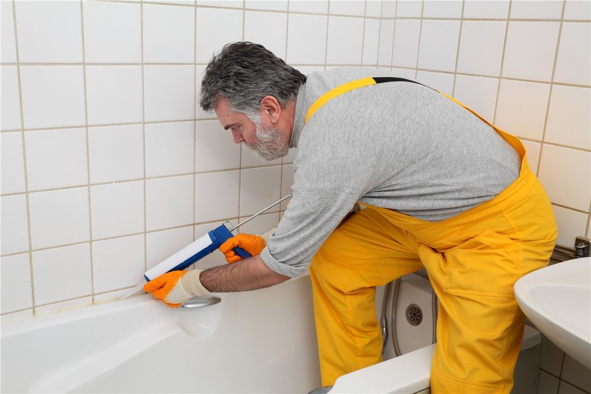 A man in yellow overalls is cleaning a bathtub in a bathroom.