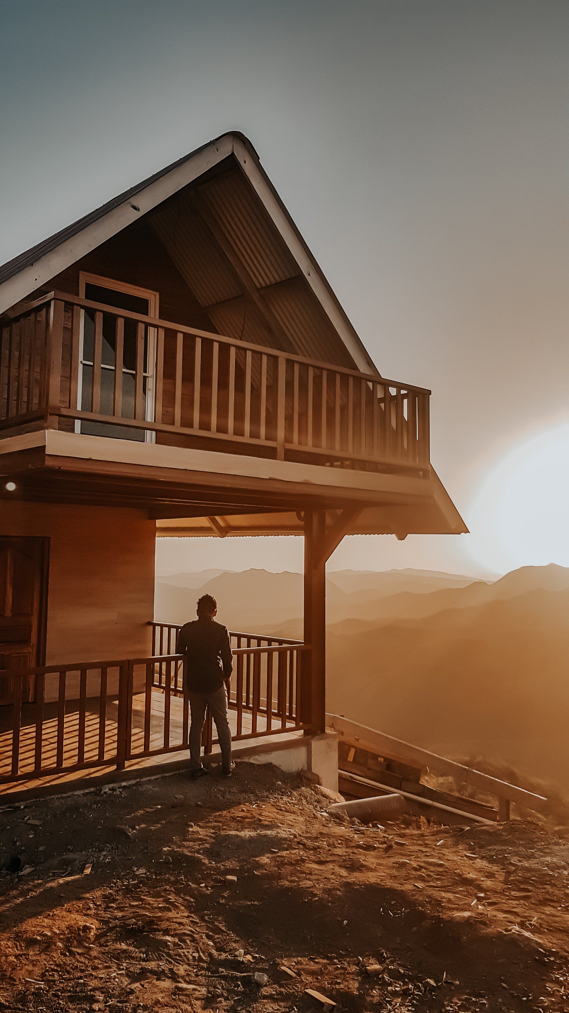 A man is standing on a balcony of a house looking at the sunset.