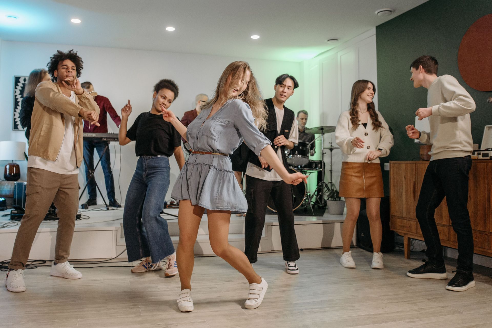 People dancing in a bright studio, with one person in a gray dress centered in front.