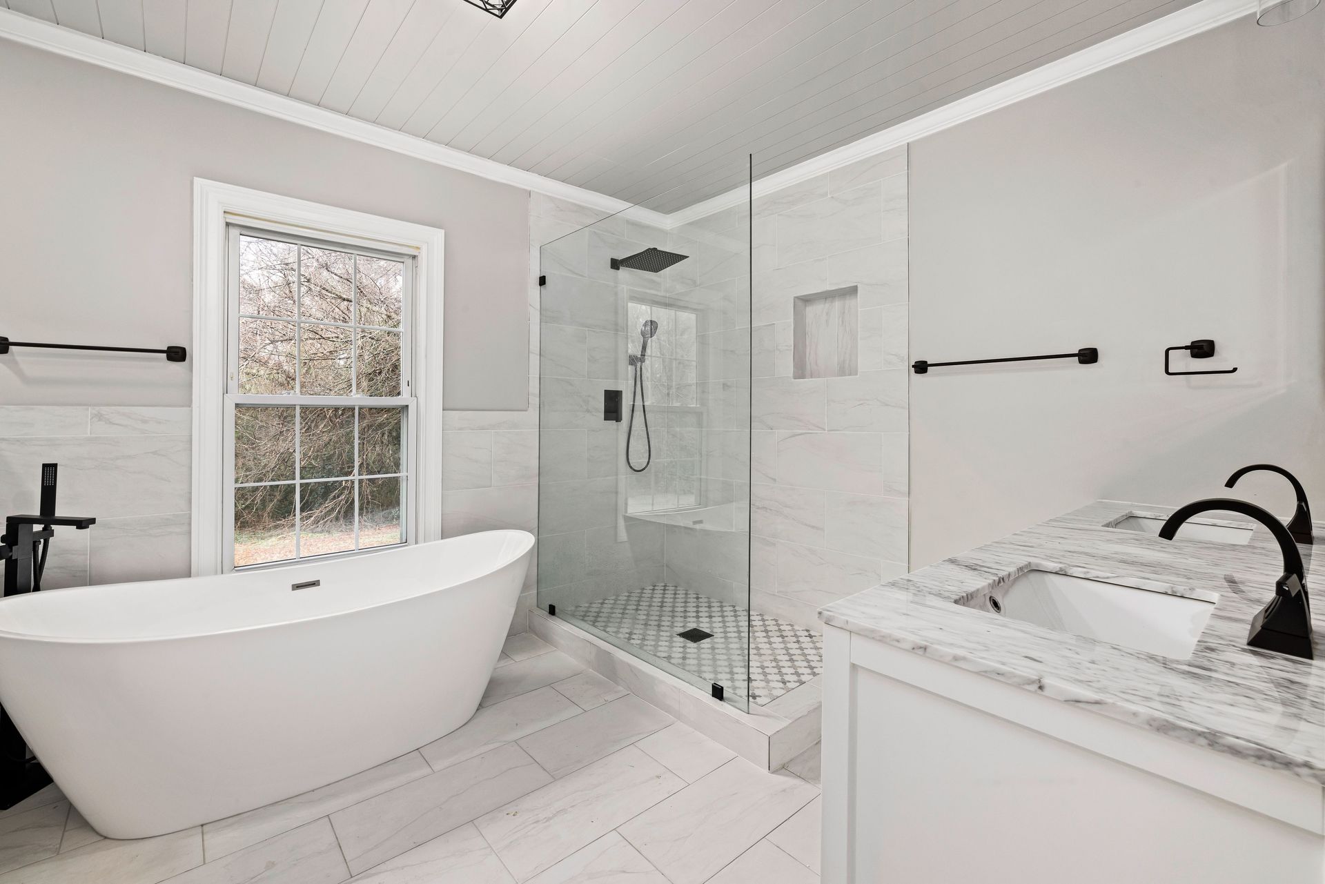 Bright modern bathroom with freestanding tub, glass shower, marble vanity, and black fixtures.