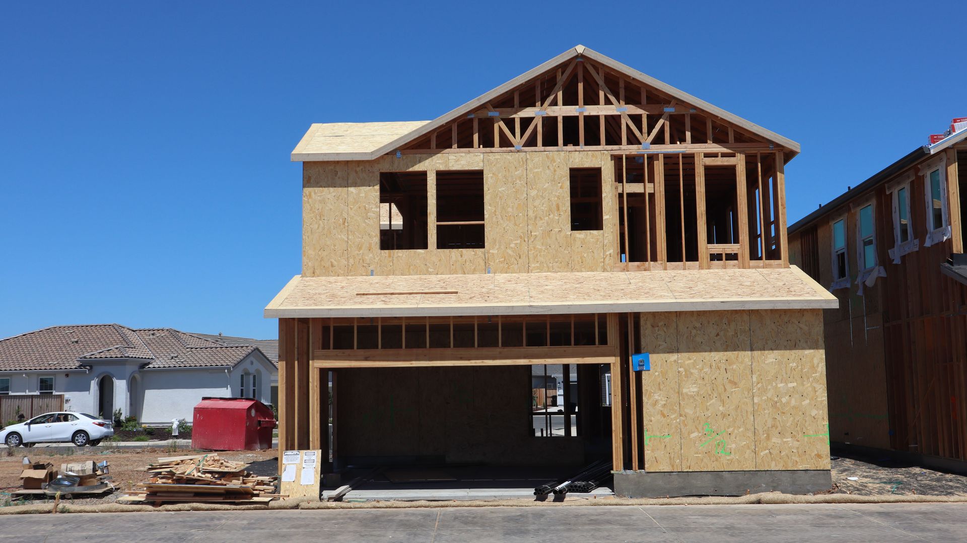 Two-story house under construction with exposed wood framing and OSB siding, on a clear day.