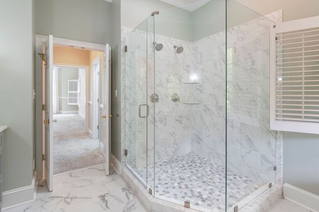 Bright marble bathroom with glass shower, mosaic floor, and window blinds