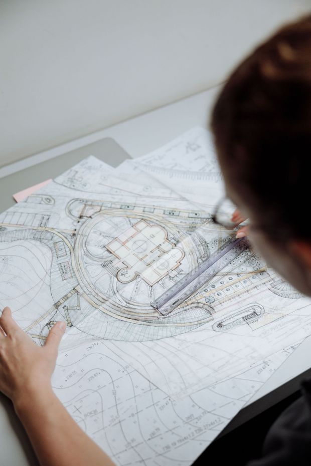 Person reviewing architectural plans on a desk, with a pencil marking details on a large blueprint