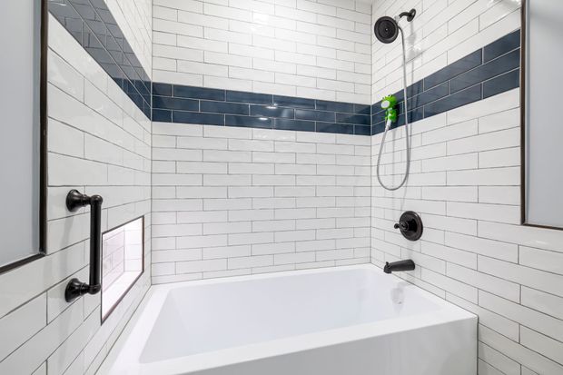 Modern white tiled bathroom shower and bathtub with black fixtures and blue accent tile strip