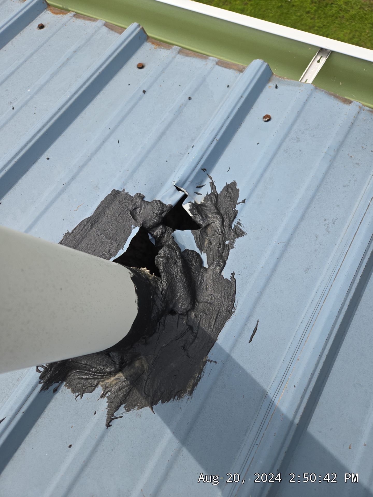 Damaged roof around a white vent pipe with torn black sealant on light blue metal roofing