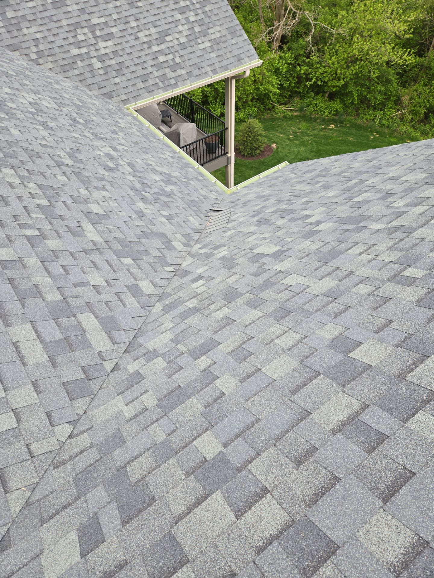 Gray shingled roof with a valley near a green yard and a small covered porch below